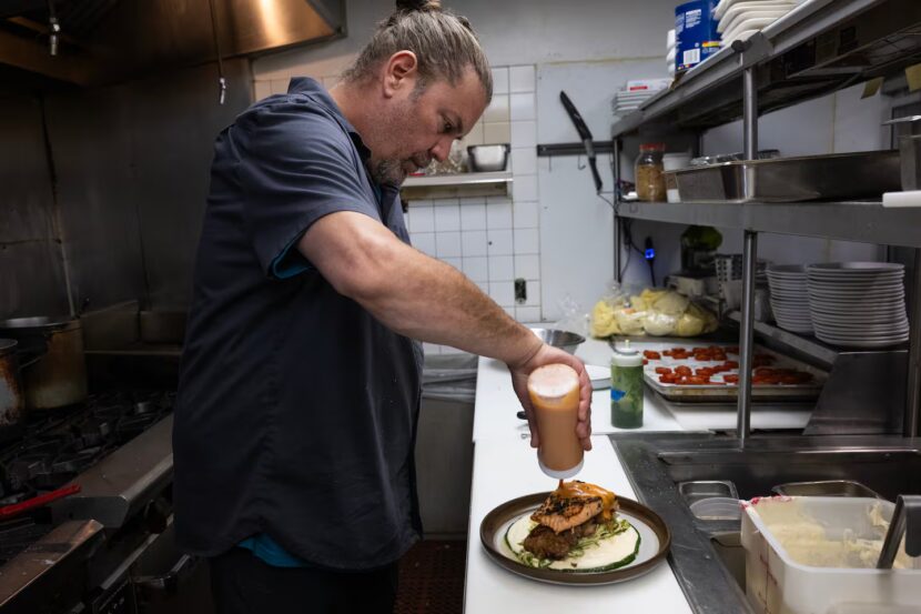 A chef tops a salmon dish with sauce