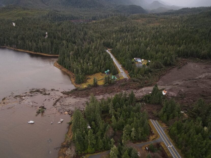 A muddy landslide path crosses a road into the ocean