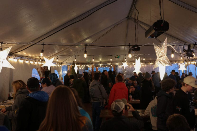 A crowd of people mingle in a white tent filled with string lights and star-shaped lights.