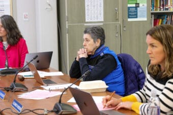 Deedie Sorensen sits with her hands clasped on a wooden table with Juneau School District Chief of Staff Kristen Bartlett to her left and Board Vice President Elizabeth Siddon to her right.