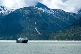 An Alaska state ferry in front of a steep mountain on a cloudy day