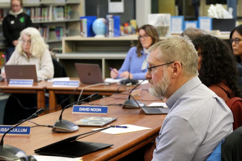 Steve Whitney sits in front of a partially closed laptop on a wooden table with his face half in view.