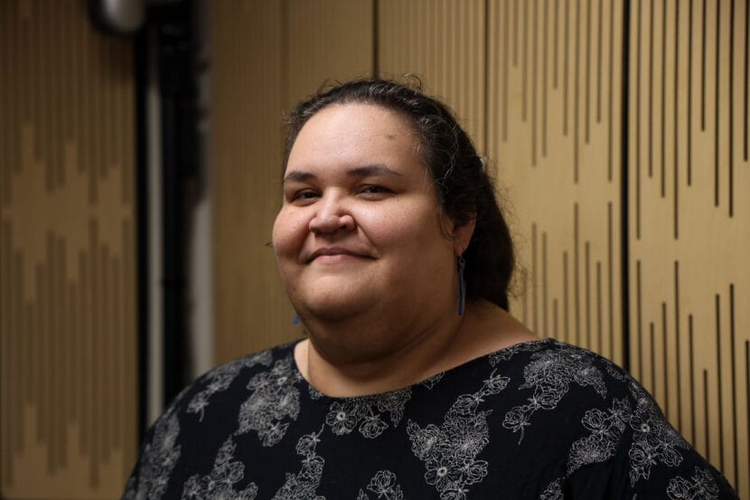 Vera Starbard poses at a slight side profile wearing blue earring and a black dress.