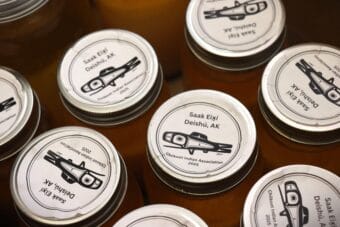 The tops of several canning jars, labeled with stickers showing a formline illustration of a fish and the words "Saak Eix̲í"