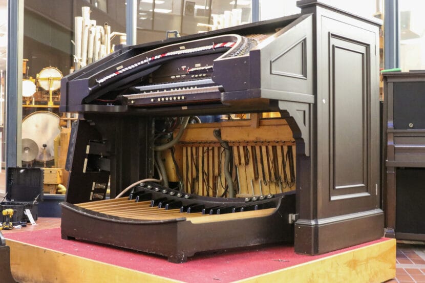 a brown wooden keyboard portion of a theater organ with a lower panel removed that reveals wooden and wired components.