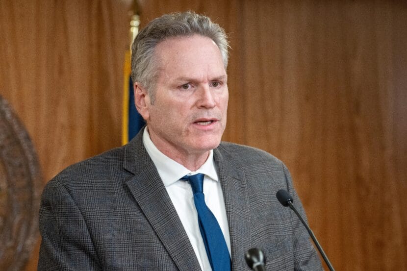 Man in grey suit standing behind microphones