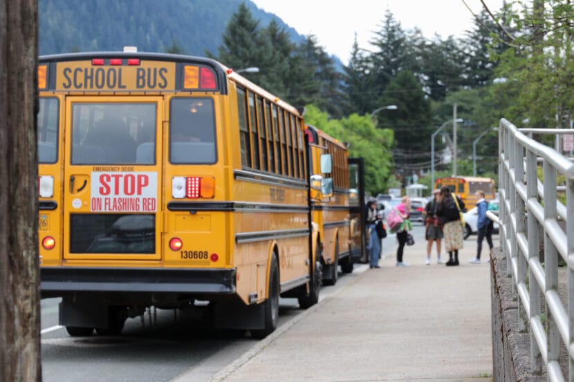 A group of students in the distance gather after exiting a yellow school bus.