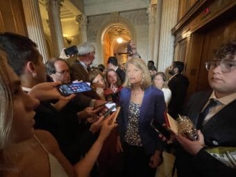 woman surrounded by people extending their iphones to her, aimed at her face