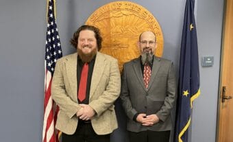 two men smiling in front of state seal