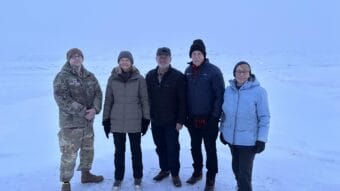 Five people in a snowy landscape, one in a military uniform