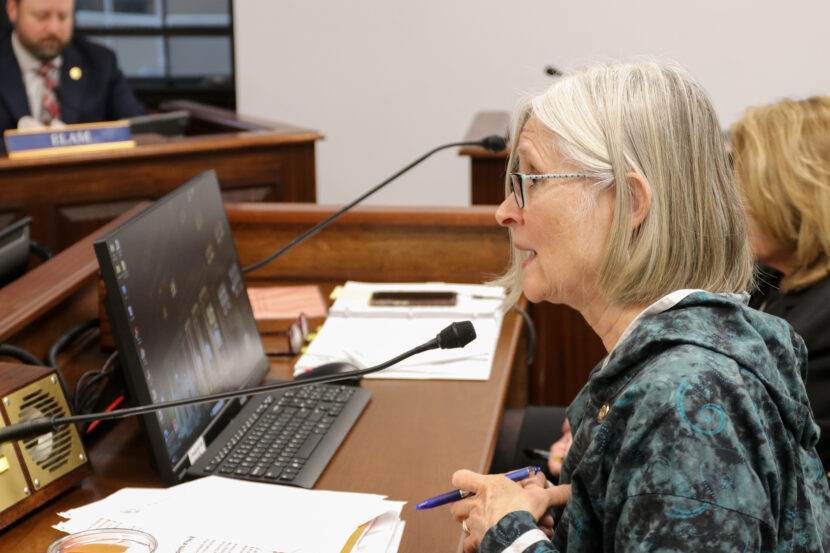Andi story speaks into a microphone in front of a wooden table.
